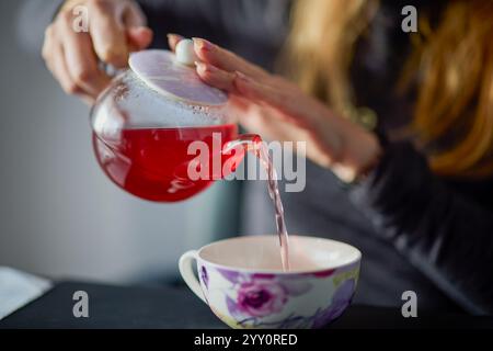 le mani di una donna versano il tè in una tazza da una teiera Foto Stock