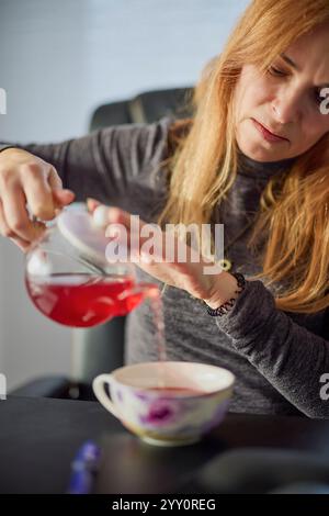 le mani di una donna versano il tè in una tazza da una teiera Foto Stock