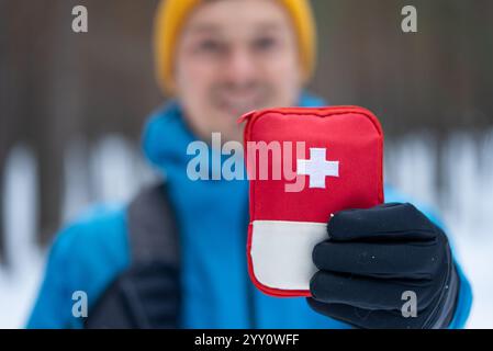 Escursionista sorridente che indossa i guanti mostrando il kit di pronto soccorso mentre cammina in una foresta invernale innevata, preparandosi a incidenti ed emergenze durante le attività all'aperto Foto Stock