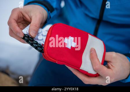 Primo piano di un alpinista che prende la medicina da un kit di pronto soccorso durante una spedizione invernale, evidenziando l'importanza della preparazione e delle forniture mediche nelle avventure all'aperto Foto Stock