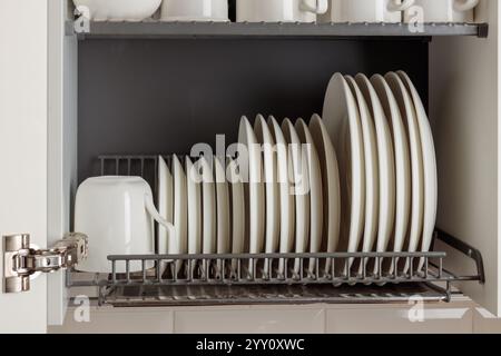 Un elegante rack in metallo per asciugare i piatti è perfettamente integrato in un armadio a parete in una cucina moderna. Il rack può contenere utensili da cucina, piatti e tazze in ceramica bianca Foto Stock