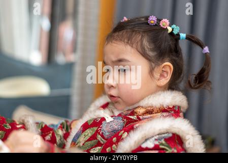 Primo piano ritratto di una piccola ragazza multirazziale in abito cinese tradizionale, pronta per festeggiare il Capodanno cinese. Sta posando per una foto Foto Stock