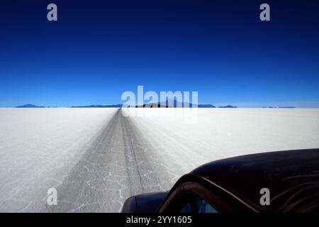 Guida su un percorso rettilineo attraverso la vasta distesa bianca delle saline del Salar de Uyuni in Bolivia, con montagne lontane. Foto Stock