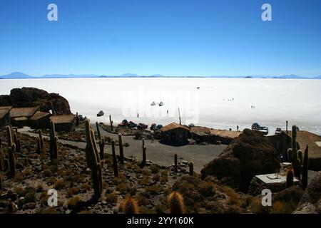 La vasta distesa bianca delle saline del Salar de Uyuni in Bolivia, con diversi veicoli e persone sparsi per il paesaggio. Foto Stock