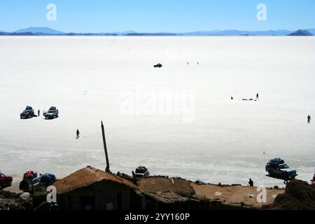 La vasta distesa bianca delle saline del Salar de Uyuni in Bolivia, con diversi veicoli e persone sparsi per il paesaggio. Foto Stock