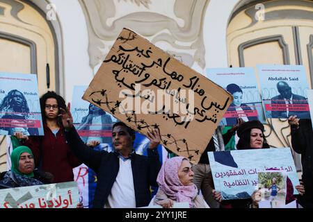 Tunisi, Tunisia, 18 dicembre 2024. Attivisti e manifestanti si riuniscono fuori dal teatro in viale Habib Bourguiba chiedendo diritti per i migranti che intraprendono il pericoloso attraversamento del Mediterraneo per raggiungere l'Italia e l'Europa. I partecipanti hanno denunciato il trattamento dell'Italia nei confronti dei migranti irregolari che raggiungono le sue coste, gli accordi della Tunisia con l'Italia e l'UE per arginare il flusso di arrivi irregolari in Europa e il "nuovo Patto sull'immigrazione e l'asilo” dell'UE. La manifestazione ha coinciso con la giornata internazionale dei migranti Foto Stock