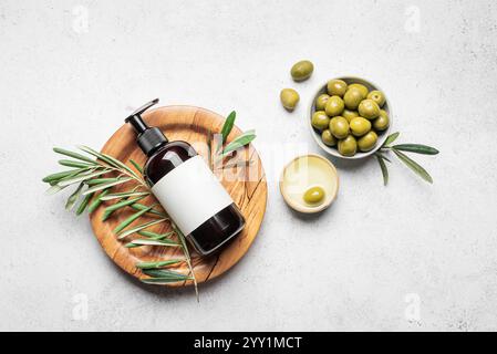 Olio d'oliva lozione per le mani e il corpo con olive e foglie verdi su sfondo bianco, vista dall'alto. Prodotti biologici per la cura della pelle, prodotti di bellezza a base di olio d'oliva. Foto Stock