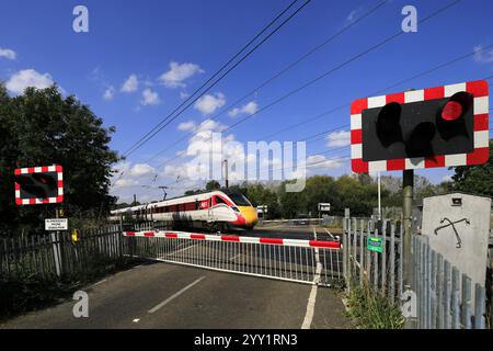 Un treno Azuma che passa a luci rosse a un passaggio a livello senza equipaggio, East Coast Main Line Railway, Peterborough, Cambridgeshire, Inghilterra, Regno Unito Foto Stock