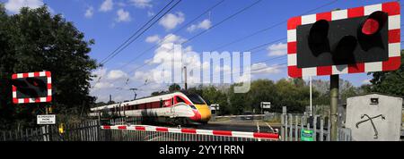 Un treno Azuma che passa a luci rosse a un passaggio a livello senza equipaggio, East Coast Main Line Railway, Peterborough, Cambridgeshire, Inghilterra, Regno Unito Foto Stock