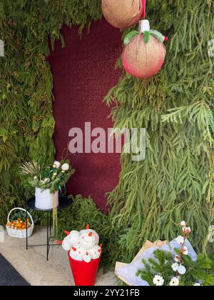 Questa foto cattura un'esposizione invernale natalizia ambientata su uno sfondo rosso intenso, circondato da lussureggianti rami di abete verde. Due ornamenti sovradimensionati Foto Stock