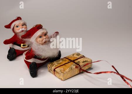 Due personaggi di babbo natale seduti con un regalo di natale su sfondo bianco, babbo natale sta arrivando al concetto di città con spazio per il testo Foto Stock