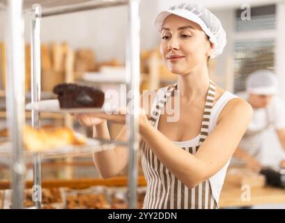 panettiera che mette in mostra una fetta di torta al cioccolato in un panificio Foto Stock