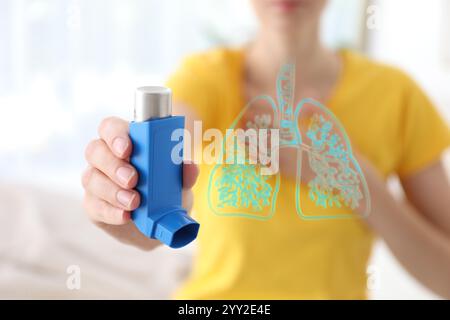 Donna con inalatore per asma in casa, concentrazione selettiva. Illustrazione dei polmoni Foto Stock