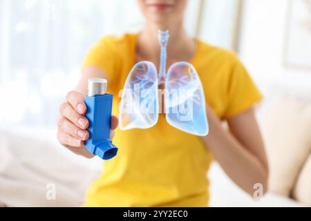 Donna con inalatore per asma in casa, concentrazione selettiva. Illustrazione dei polmoni Foto Stock