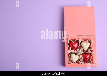 Gustose caramelle al cioccolato a forma di cuore su sfondo viola, vista dall'alto con spazio per il testo. Buon San Valentino Foto Stock