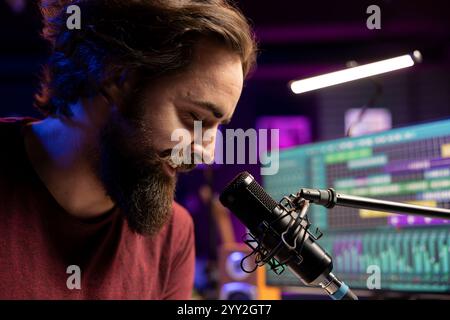 Compositore musicale che canta i suoi nuovi testi al microfono in studio domestico, producendo colonne sonore con interfaccia software daw su pc. Artista maschile che compone una nuova melodia con console di mixaggio. Primo piano. Foto Stock