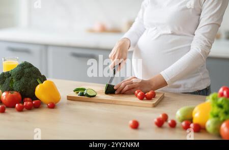 Donna incinta prepara verdure fresche in cucina soleggiata per un pasto sano Foto Stock