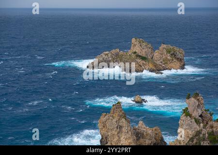 Una piccola isola rocciosa solitaria in mare aperto. Tempesta in mare, onde infurianti che si infrangono contro la piccola isola ed esplodono con spruzzi bianchi. Rock in A. Foto Stock