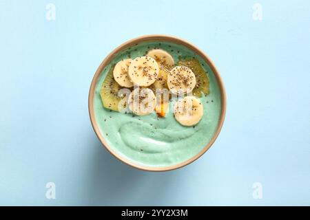 Ciotola con saporito frullato di spirulina, banana, kiwi e semi di chia su sfondo blu Foto Stock