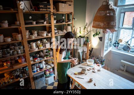 Una donna professionista concentrata tiene e fissa la maniglia alla tazza di argilla, fissando il materiale Foto Stock