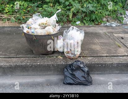 La vista frontale della spazzatura in un sacchetto di plastica nero sul deposito dei rifiuti sul lato della strada o sul sentiero si trova nel centro città. Foto Stock