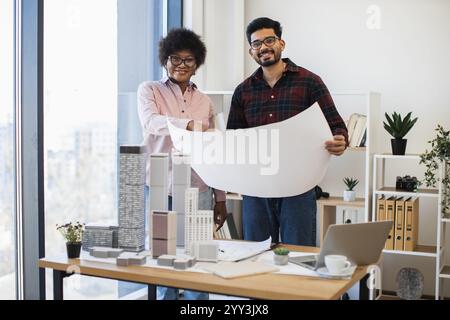 Architetti indiani e donne africane che analizzano i progetti per il progetto di sviluppo della città. Lavoro di squadra creativo in un ambiente moderno. Lavoro collaborativo con modelli di edifici, impianti e vista città. Foto Stock