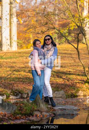 Felice mamma single e sua figlia adolescente a piedi nel parco autunnale. Mamma abbraccia e bacia amorevolmente la ragazza. Maternità. Giornata della famiglia. Tempo insieme. Vuoto attivo Foto Stock