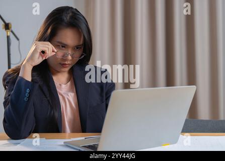 Preoccupata, stanca, donna d'affari matura che indossa gli occhiali, che ha mal di testa al lavoro. Giovane donna d'affari stanca e affollata che sente lo stress sul posto di lavoro che guarda Foto Stock