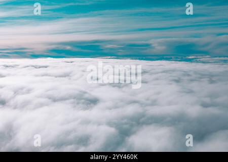 Vasta distesa di nuvole vista dall'alto da un aereo. Sopra le nuvole, il cielo è visibile con un gradiente di tonalità blu e grigie, che indica var Foto Stock