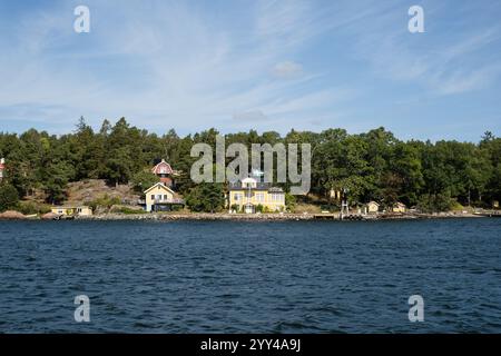 Vista di una casa gialla con una bandiera svedese che sventola, dall'arcipelago di Stoccolma dal traghetto Waxholmsbolaget, Svezia Foto Stock