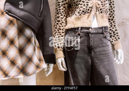 Un elegante espositore con due manichini vestiti con abiti alla moda, che mostra un mix di texture e stili, tra cui un cappotto e jeans in pelliccia sintetica. Foto Stock