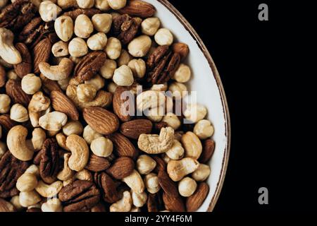 Un delizioso assortimento di noci miste tra cui mandorle, noci pecan, nocciole e anacardi in una ciotola decorativa su sfondo scuro, perfetta per sane Foto Stock