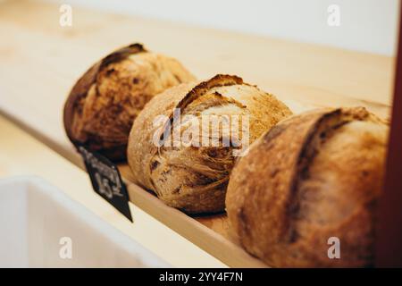 Una selezione di pane artigianale appena sfornato esposto su uno scaffale rustico in legno in una panetteria, che mostra le loro croste dorate e croccanti e l'aroma invitante Foto Stock