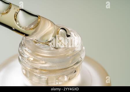Vista ravvicinata di un contagocce riempito di liquido trasparente posizionato su una bottiglia di vetro. Il liquido, probabilmente siero o olio, enfatizza la cura della pelle e la purezza. Foto Stock