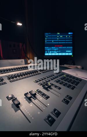 Primo piano di un mixer audio professionale in uno studio poco illuminato. I comandi e i cursori illuminati creano un'atmosfera suggestiva per un audio coinvolgente Foto Stock