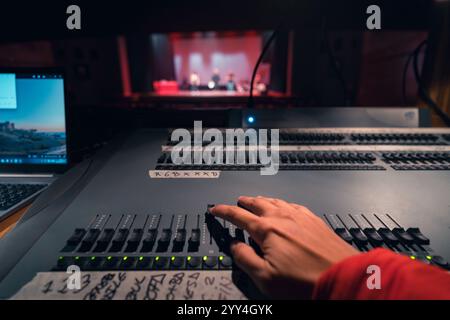 Una mano regola il controllo su una scrivania illuminata da teatro, migliorando l'atmosfera del palcoscenico. Il palco è poco visibile sullo sfondo, mostrando un'esibizione dal vivo Foto Stock