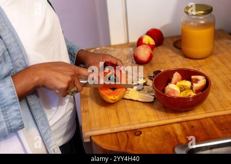 Una persona affetta una papaia matura su un asse di legno, circondato da pesche e banane. Un bicchiere di succo si trova nelle vicinanze. Perfetto per illustrare un pasto sano Foto Stock