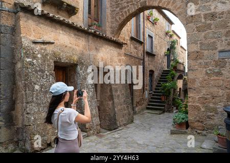 Un turista in una berlina bianca fotografa un affascinante vicolo in pietra in un villaggio italiano. La scena include edifici rustici, arcate, piante in vaso e c Foto Stock