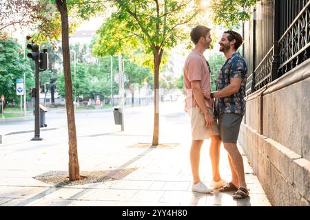 Una coppia gay condivide un momento di gioia su un marciapiede soleggiato della città, sorridendo e abbracciando calorosamente Foto Stock