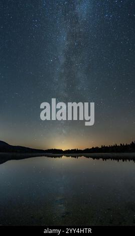 Splendida vista della via Lattea che si riflette sul Lac de Bellefontaine di notte, le montagne del Giura francese offrono uno sfondo sereno a questa sce celeste Foto Stock