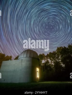 Splendida foto a lunga esposizione di sentieri stellari che circondano Polaris sopra l'Osservatorio di Ginevra in Svizzera, con una finestra illuminata e alberi di nuovo sagomati Foto Stock