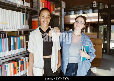 Ritratto di una giovane donna sorridente in piedi con la mano sulla spalla di un'amica nella biblioteca universitaria Foto Stock