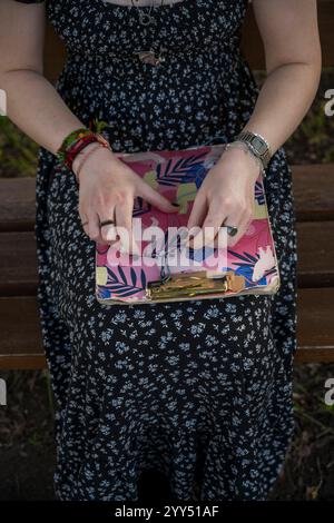 Primo piano tra le mani di una giovane donna seduta su una panchina del parco è il filetto di cotone delle perle per rendere disponibile un braccialetto Foto Stock