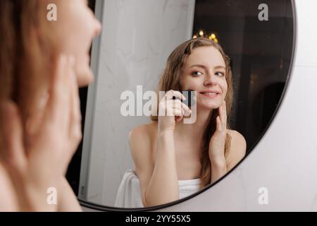 Cura della pelle anti-invecchiamento. Donna sorridente di mezza età massaggiando il collo con lo strumento gua Sha, attraente donna matura che fa un trattamento di sollevamento della pelle con giada guas Foto Stock