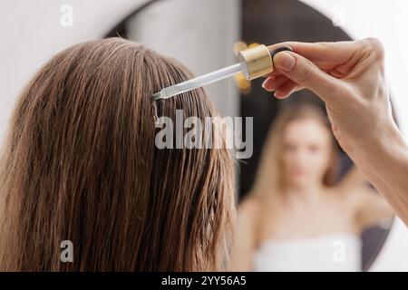 Giovane donna che applica olio essenziale organico naturale su capelli e pelle. Centro benessere e rituali di bellezza. Cura della pelle. Foto Stock