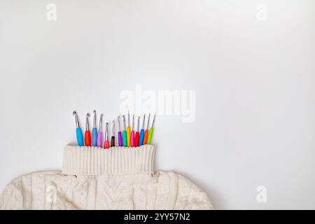 Un primo piano di accessori all'uncinetto, tra cui ganci e filati su un morbido sfondo maglione, con un'iscrizione creativa "Crochet" in filato, Symboliz Foto Stock