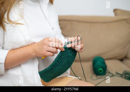 Un primo piano di accessori all'uncinetto, tra cui ganci e filati su un morbido sfondo maglione, con una creativa scritta "Crochet" fatta di filati e mani Foto Stock