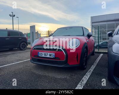 Parigi, Francia - 5 dicembre 2024: Una mini Cooper rossa smerigliata parcheggiata all'alba in una concessionaria, con condensa visibile sulla sua superficie, sullo sfondo di un cielo mattutino limpido Foto Stock