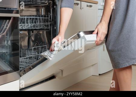 Donna che pulisce le mani lavastoviglie vuota incorporata con lo sportello aperto con un asciugamano o uno straccio. Cucina con mobili bianchi minimalisti nella casa moderna. Si Foto Stock