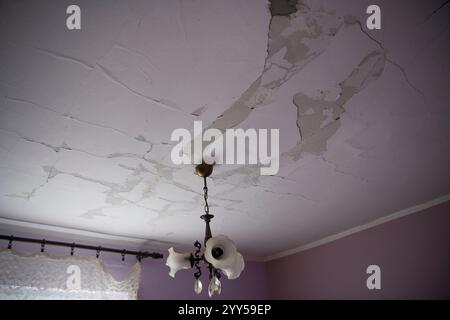 Distacco della parete di vernice dell'acqua dal soffitto dell'intonaco. Grandi zone umide e grandi fessure sul soffitto della camera domestica Foto Stock
